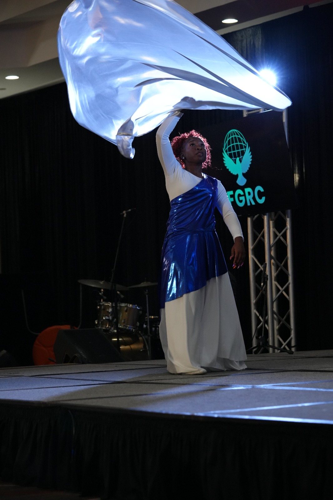 A dancer ministers with a silver worship flag onstage