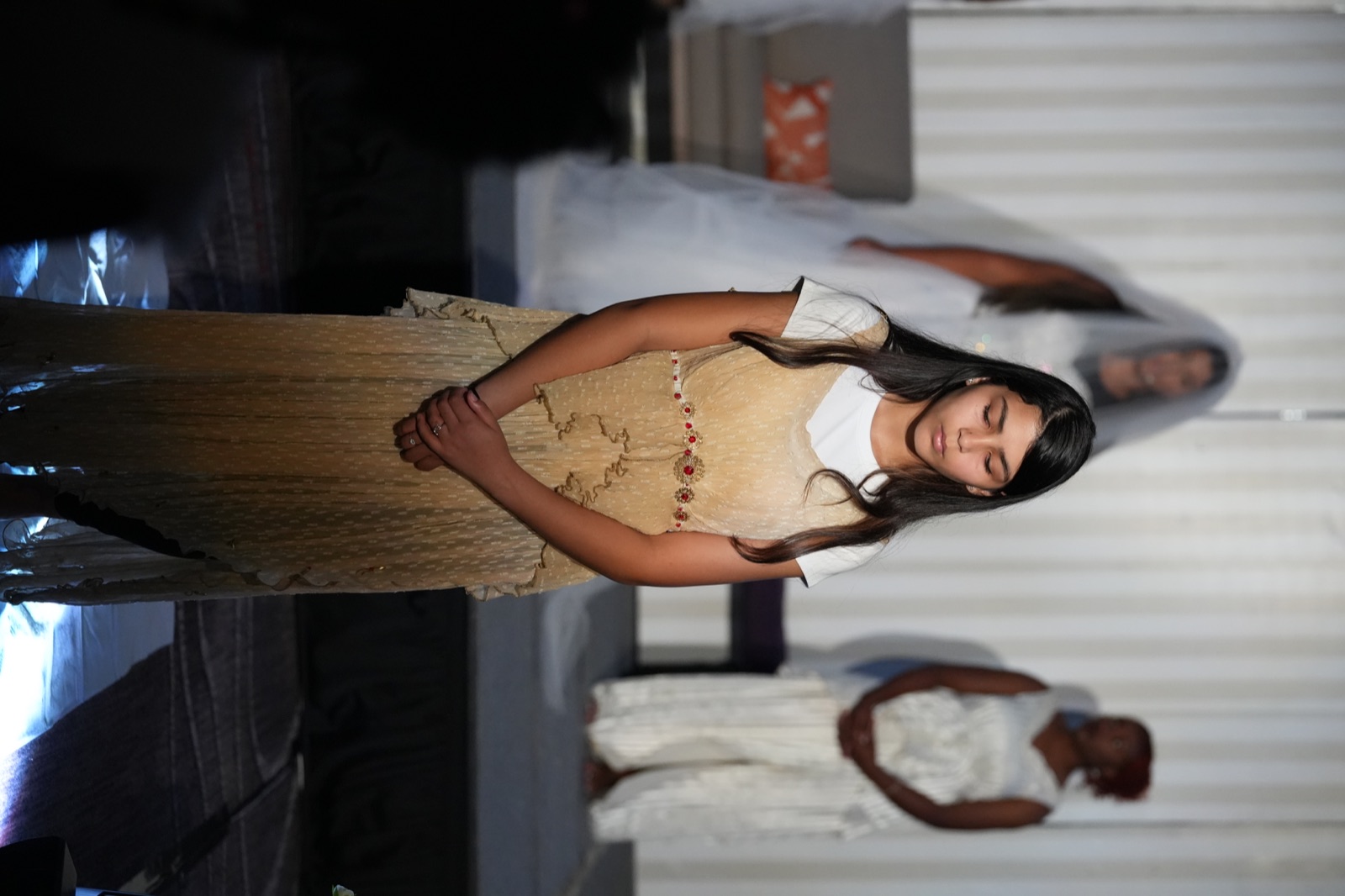 A young performer in cream and gold stands before the company