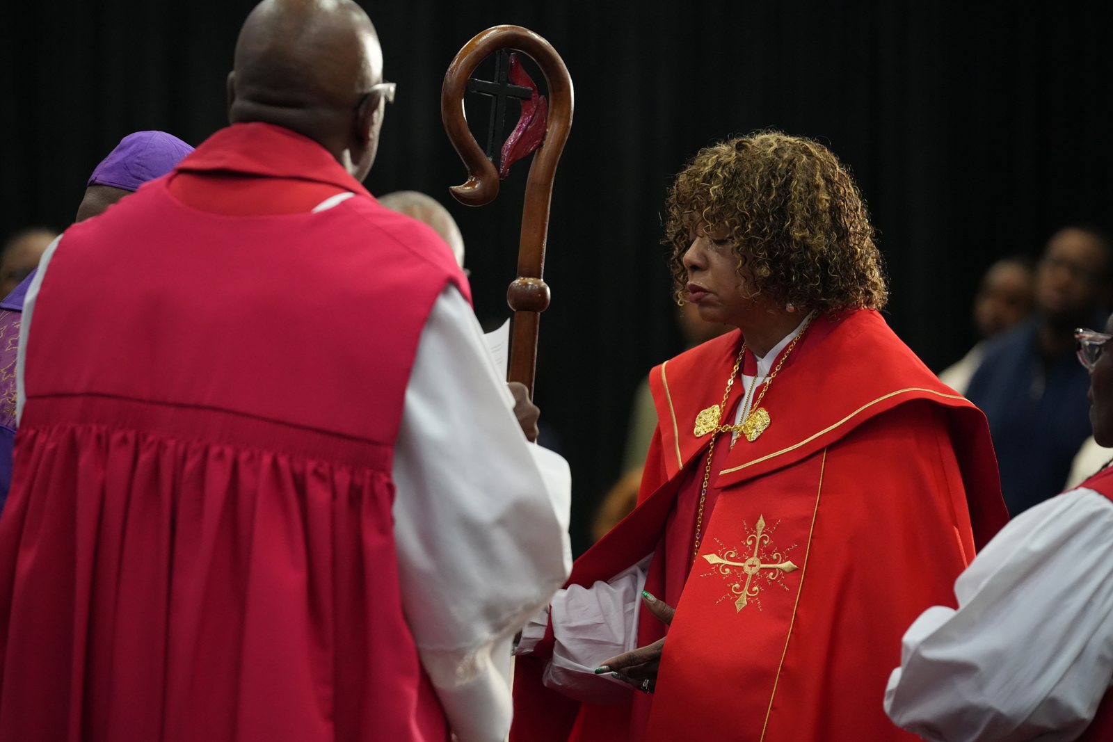 Apostle Dr. Sandra Mitchell stands in red vestments before the presbytery during her consecration