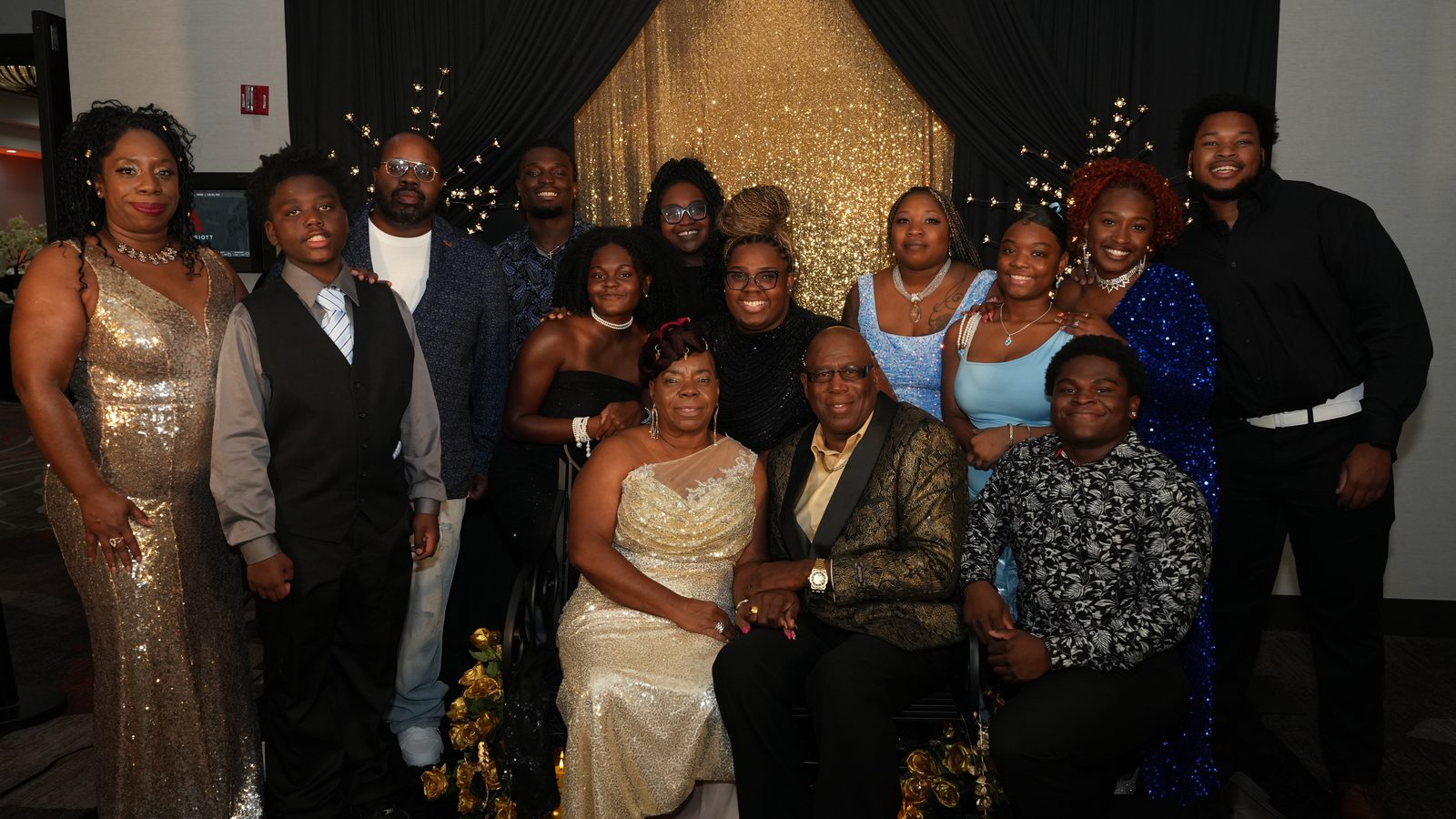 A three-generation family of fourteen in formal dress, gathered around two seated elders, at the Freedom Charity Ball