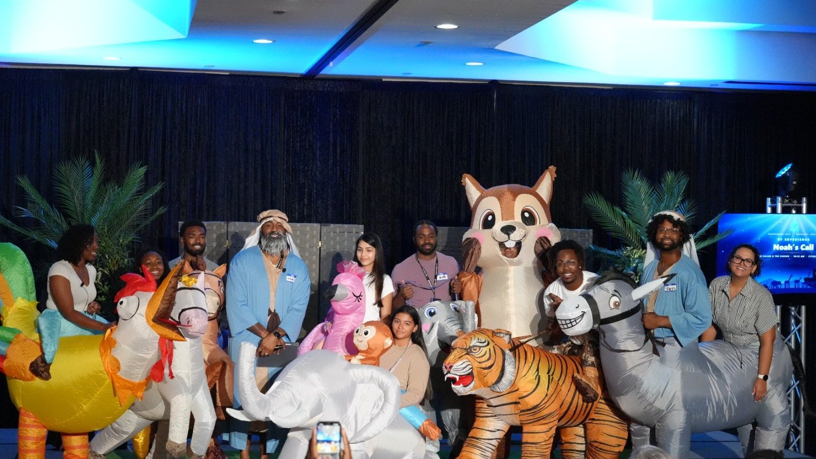 The Noah's Call company on stage in inflatable animal costumes beside Noah in his blue robe